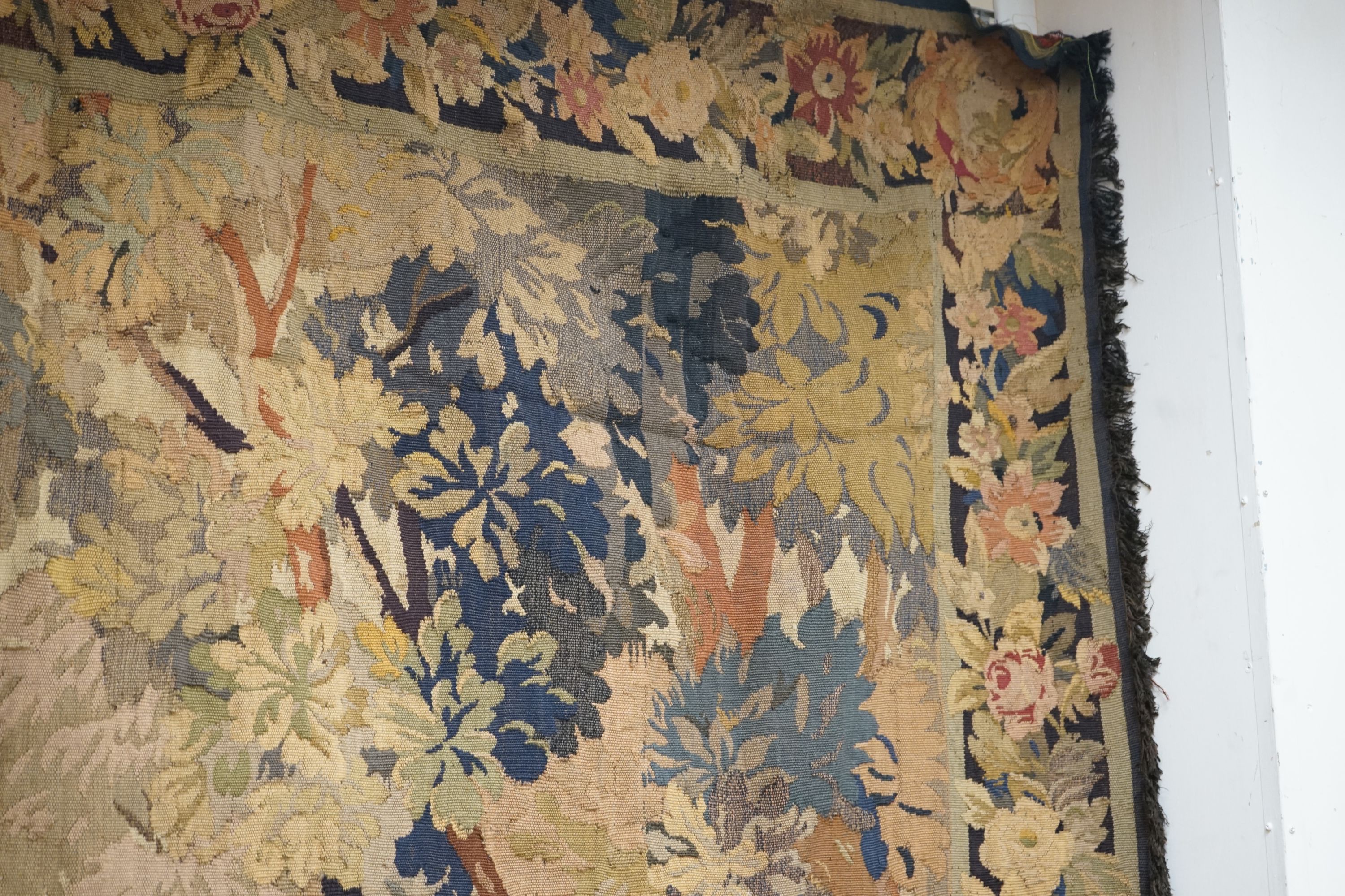 A late 19th / early 20th century French tapestry depicting a woodland scene with trees and flowers with a floral border woven in autumnal colours